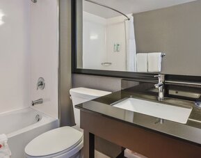 Modern guest bathroom featuring a bathtub and shower combination, contemporary vanity, and complimentary bath amenities at Comfort Inn Airport East Ancienne-Lorette.