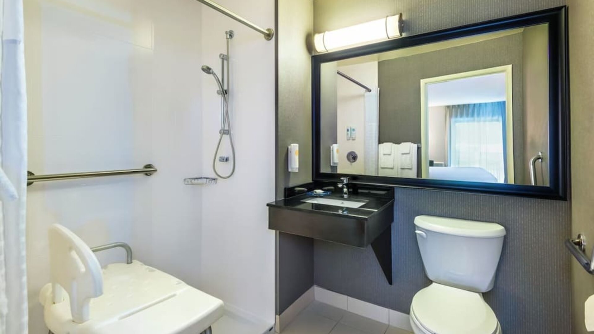 Accessible guest bathroom featuring a roll-in shower, shower seat, grab bars, and an accessible vanity at Comfort Inn Airport East Ancienne-Lorette.