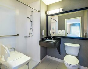 Accessible guest bathroom featuring a roll-in shower, shower seat, grab bars, and an accessible vanity at Comfort Inn Airport East Ancienne-Lorette.