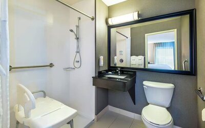 Accessible guest bathroom featuring a roll-in shower, shower seat, grab bars, and an accessible vanity at Comfort Inn Airport East Ancienne-Lorette.