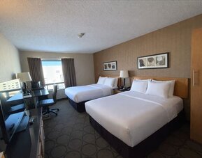 Double queen guest room offering two plush beds, workspace, flat-screen TV, and plenty of natural light at Comfort Inn Baie-Comeau.