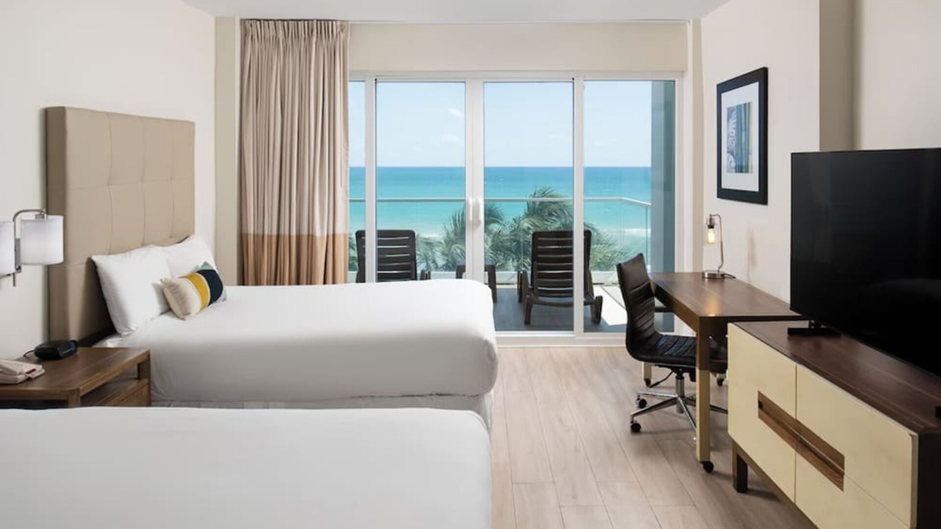 Oceanfront guest room with two beds, workspace, and private balcony at Sherry Frontenac Oceanfront Hotel.