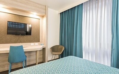 Guest room workspace with wall-mounted TV, desk, chair and floor-to-ceiling curtains at Hotel Casa Blanca.
