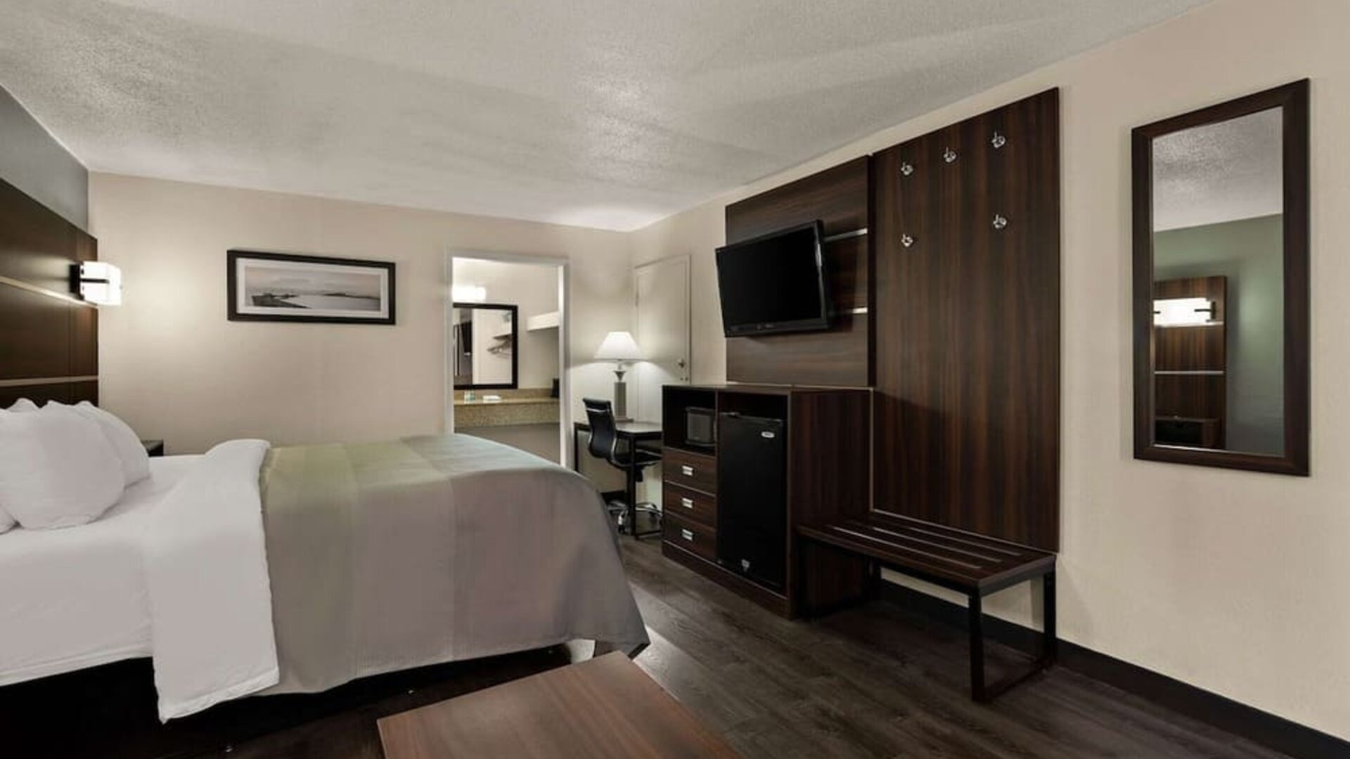 King guest room with wall-mounted TV, workspace, mini fridge and luggage bench at Quality Inn Yemassee - Point South I-95.
