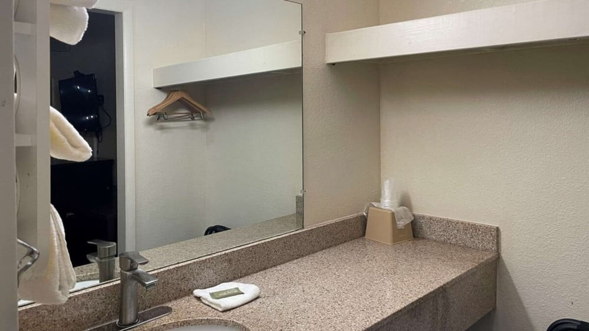 Bathroom vanity with granite countertop, large mirror, open shelving and hanging space at Econo Lodge Yemassee.
