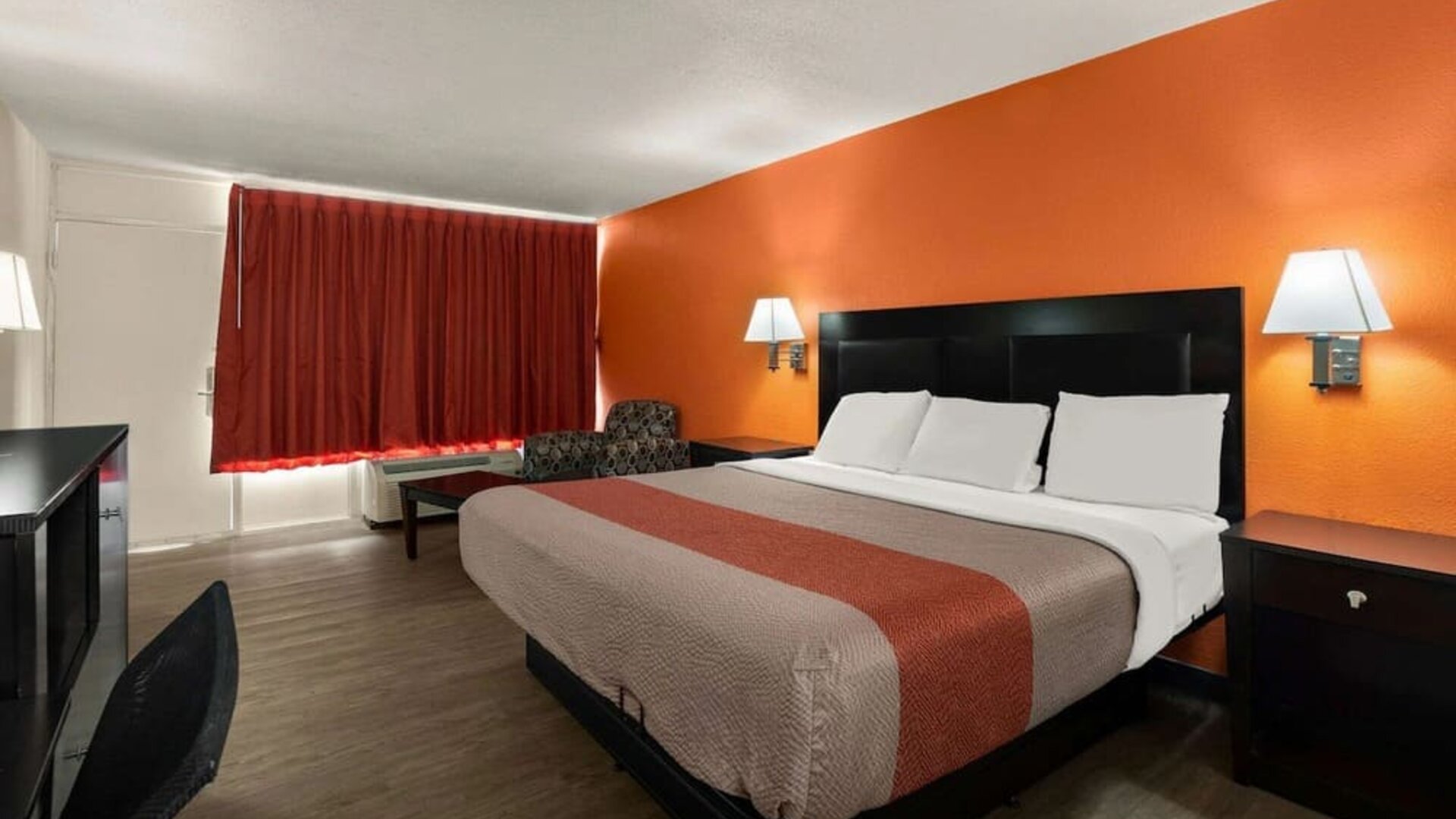 King guest room with orange accent wall, blackout curtains and workspace at Econo Lodge Yemassee.