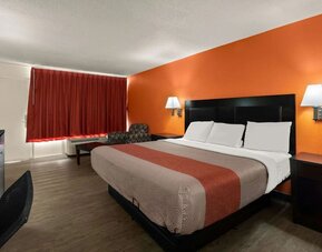 King guest room with orange accent wall, blackout curtains and workspace at Econo Lodge Yemassee.