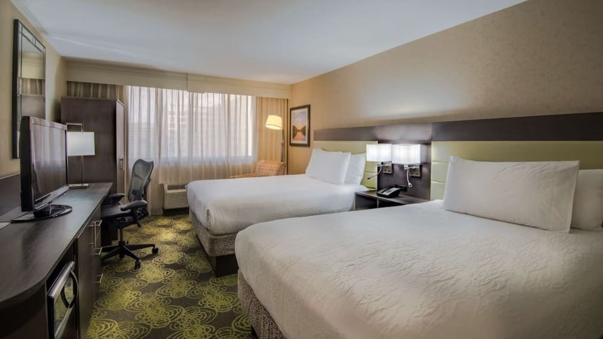 Guest room with two queen beds, HDTV, workspace, blackout curtains, and modern furnishings for a comfortable stay.
