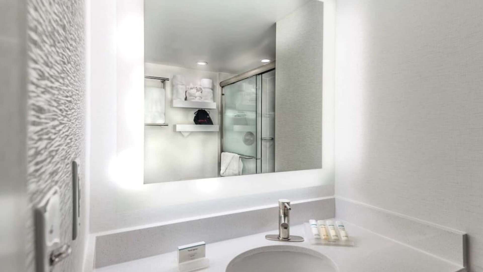 Modern guest bathroom with illuminated vanity mirror, spacious countertop, walk-in shower, and premium bath amenities.