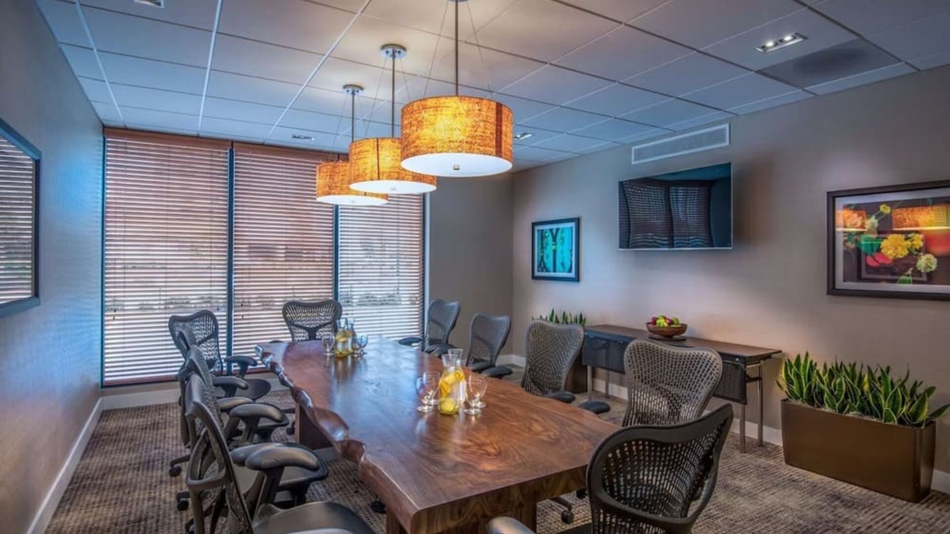 Private meeting room with large conference table, ergonomic chairs, TV, and natural light for business gatherings.