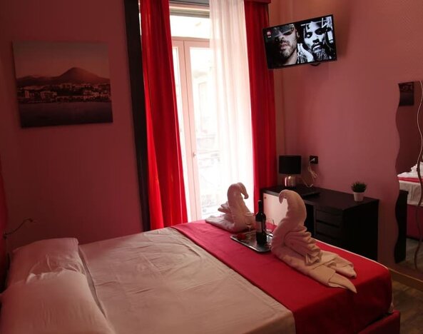 Double room with red curtains, balcony access, towel swans and wall-mounted TV at Dolce Vita Rooms & Breakfast.