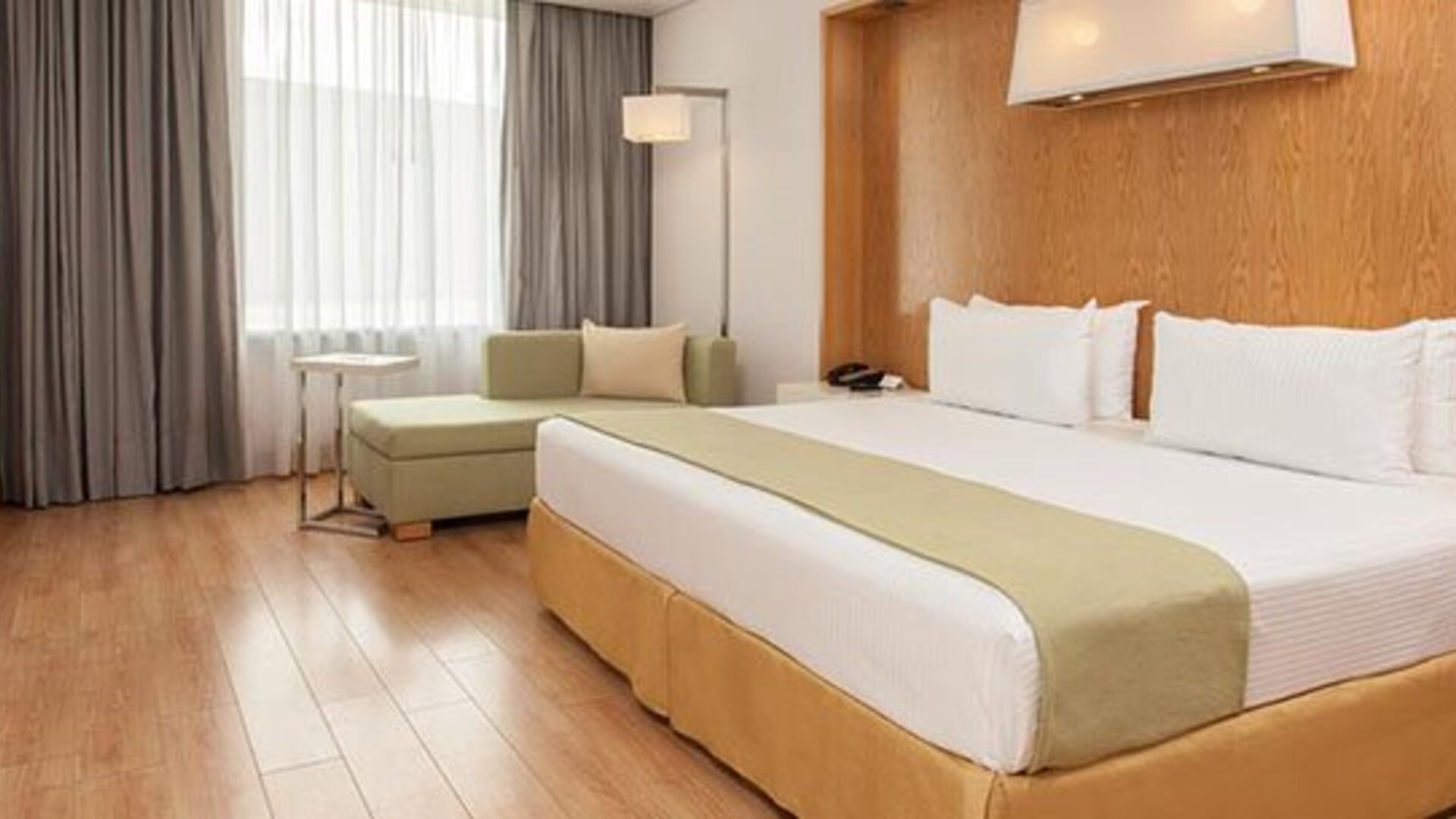 Bright guest room with king bed, chaise lounge, large windows and modern décor at NH Collection Mexico City Airport T2.