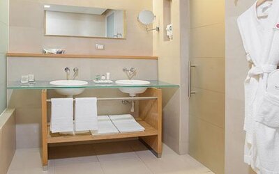 Modern bathroom with double vanity, bathtub, glass countertop and premium bath amenities at NH Collection Mexico City Airport T2.