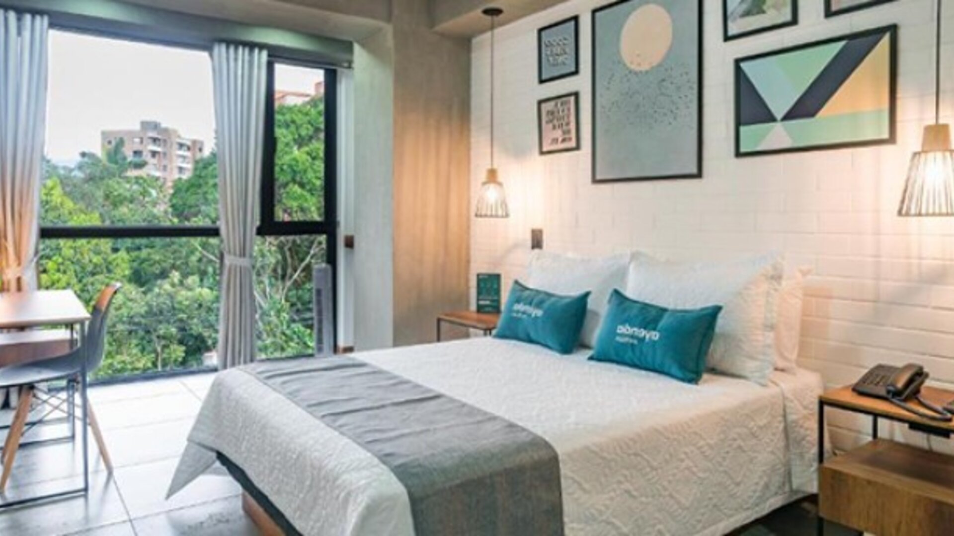 Bright guest room at Hotel Loft 32 featuring a comfortable bed, large windows overlooking greenery, workspace and contemporary décor.