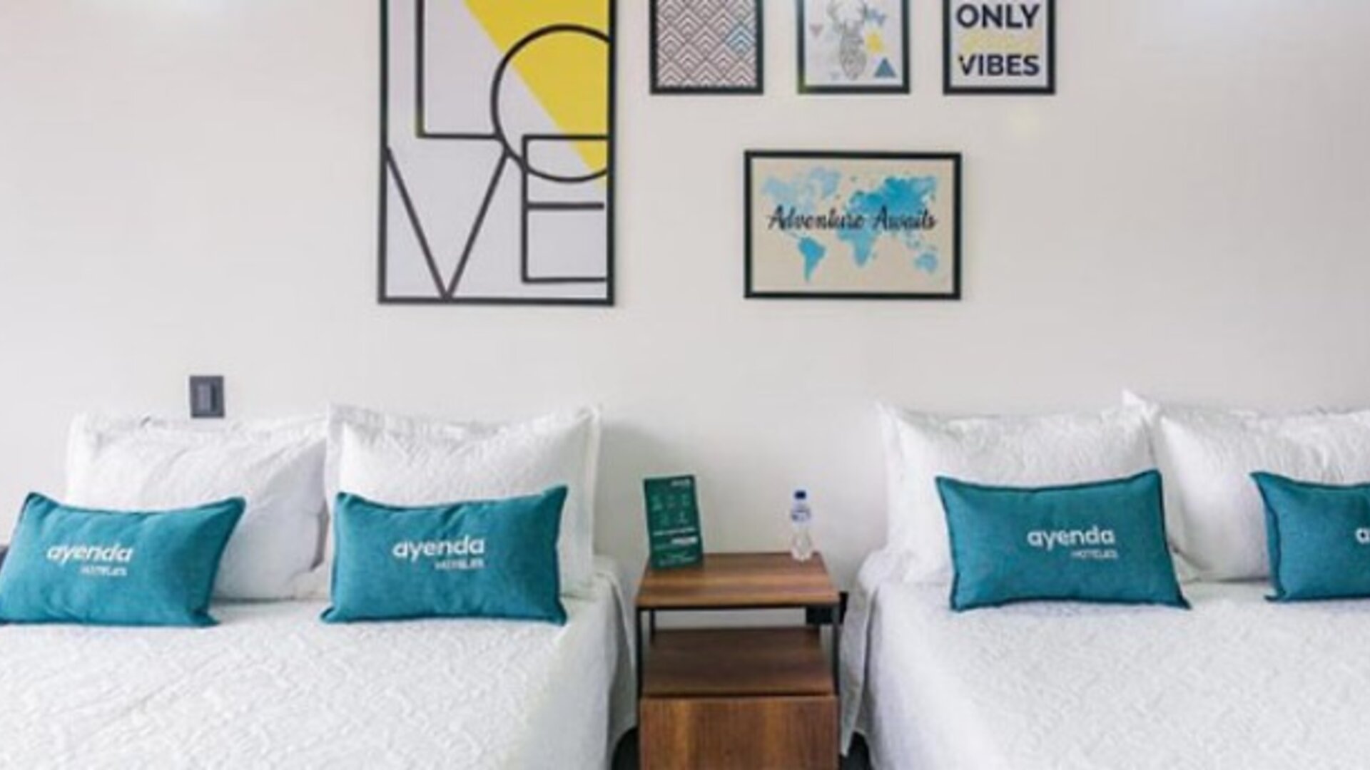 Guest room at Hotel Loft 32 featuring two beds with teal accent cushions and contemporary framed artwork.