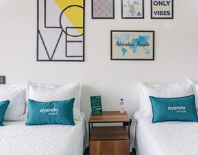 Guest room at Hotel Loft 32 featuring two beds with teal accent cushions and contemporary framed artwork.