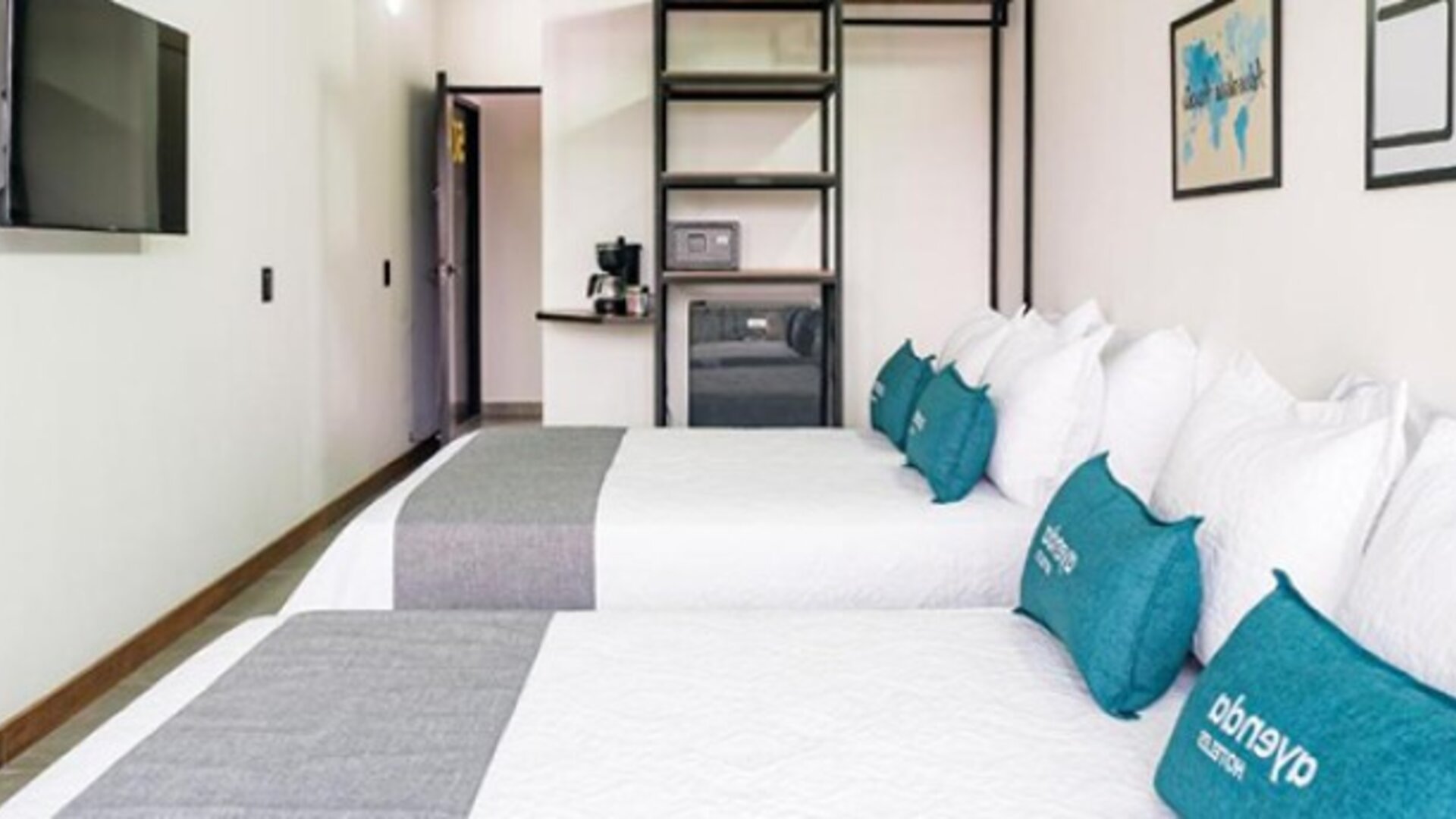 Spacious guest room at Hotel Loft 32 featuring two beds, teal accent cushions, a flat-screen TV and in-room storage.