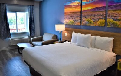 King room at Days Inn & Suites By Wyndham Downtown/University Of Houston featuring a king bed, seating area, window and colorful landscape artwork.