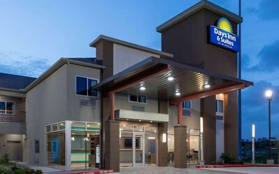 Front entrance of Days Inn & Suites By Wyndham Downtown/University Of Houston featuring a covered entrance and illuminated hotel signage.