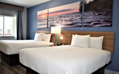Guest room at Days Inn & Suites By Wyndham Downtown/University Of Houston featuring two beds, bedside lighting and scenic wall artwork.