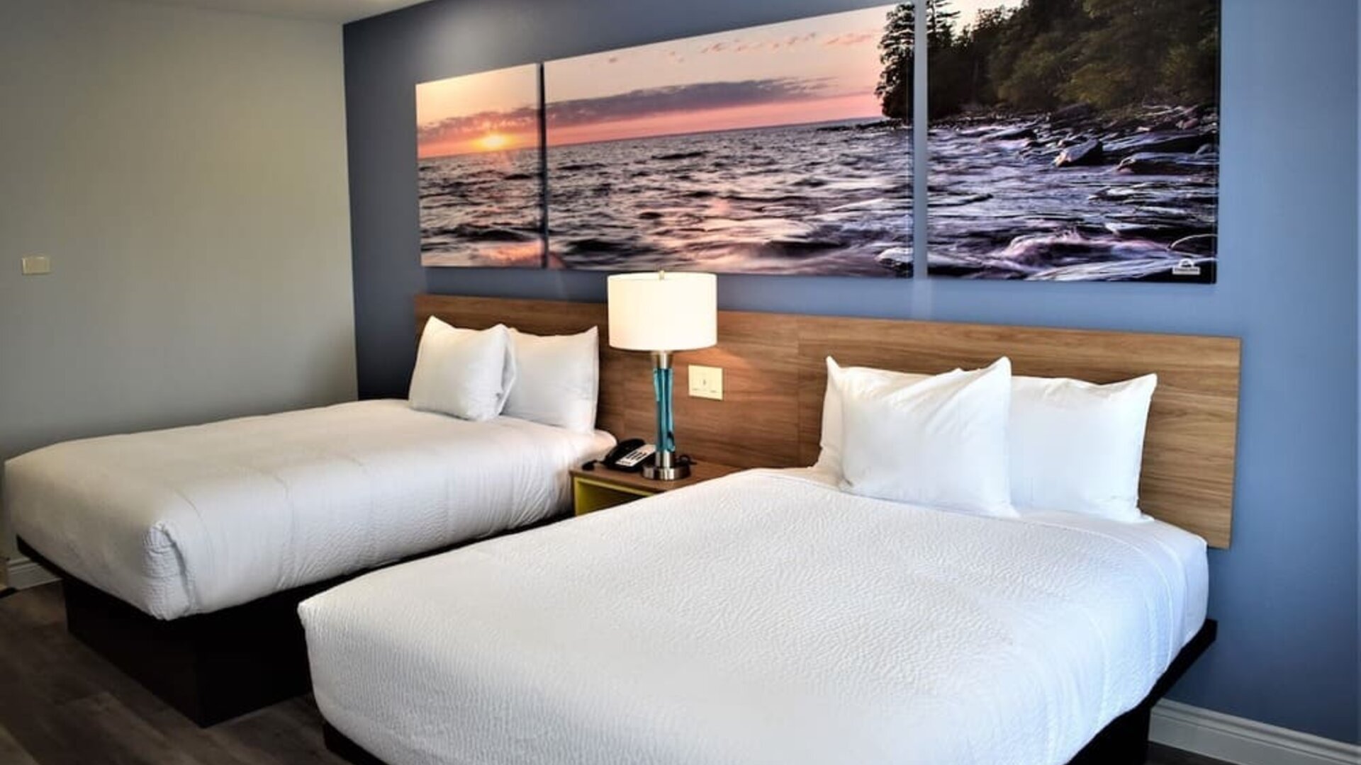 Guest room at Days Inn & Suites By Wyndham Downtown/University Of Houston featuring two beds and colorful scenic wall artwork.