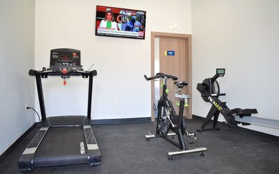 Fitness center at Days Inn & Suites By Wyndham Downtown/University Of Houston featuring a treadmill, exercise bike, rowing machine and wall-mounted TV.