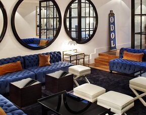 Lobby lounge at Hotel Pulitzer Buenos Aires featuring deep blue sofas, white ottomans, large round mirrors and modern furnishings.