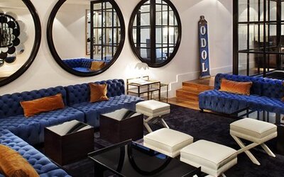 Lobby lounge at Hotel Pulitzer Buenos Aires featuring deep blue sofas, white ottomans, large round mirrors and modern furnishings.