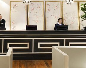 Reception desk at Hotel Pulitzer Buenos Aires featuring a sophisticated black-and-white counter, decorative wall panels and hotel staff.