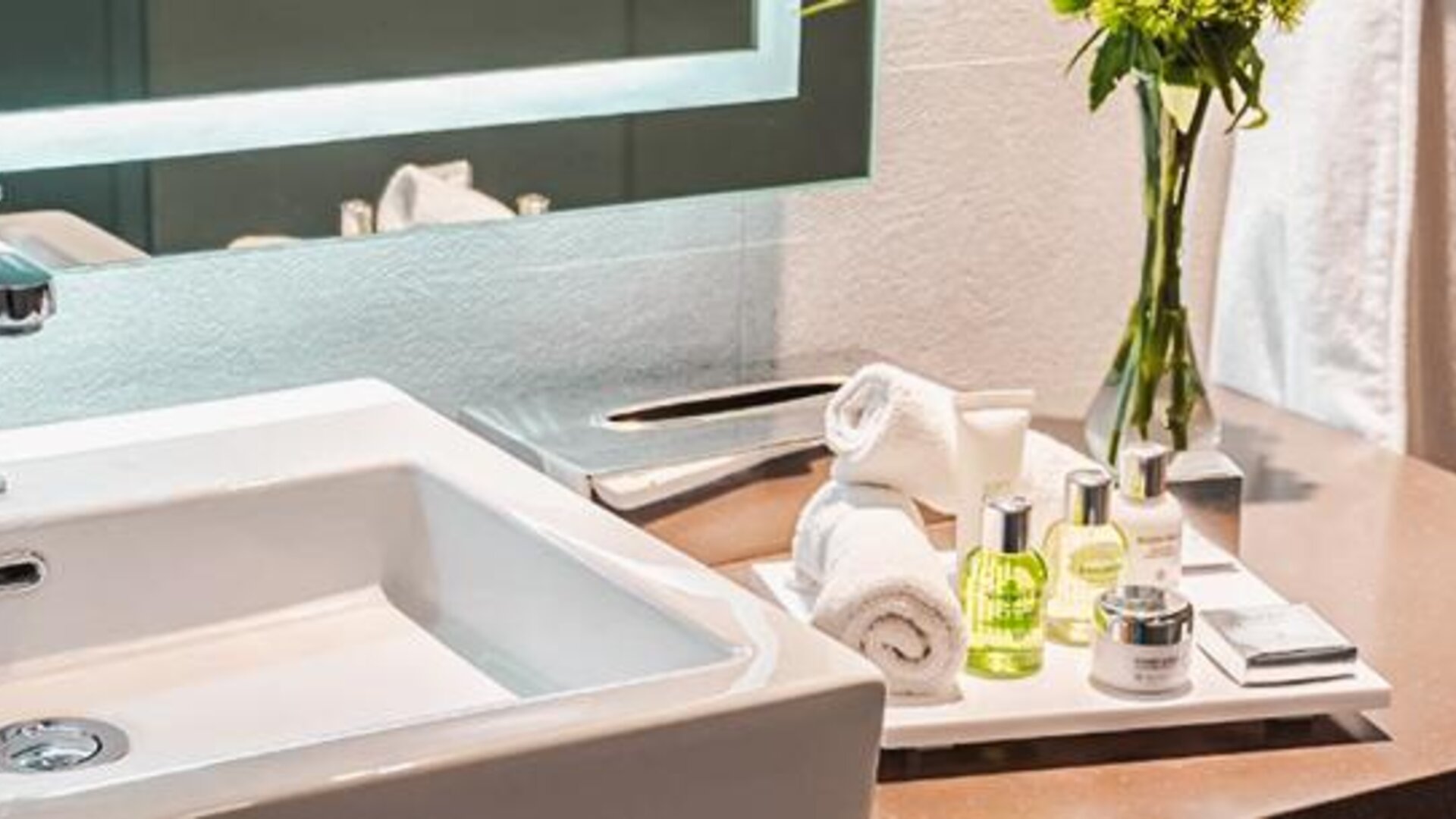 Bathroom vanity at NH Collection Mexico City Centro Histórico featuring a modern sink, illuminated mirror, fresh towels and guest amenities.