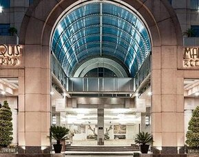 Main entrance of Hotel Marquis Reforma featuring an illuminated arched glass canopy and landscaped planters.