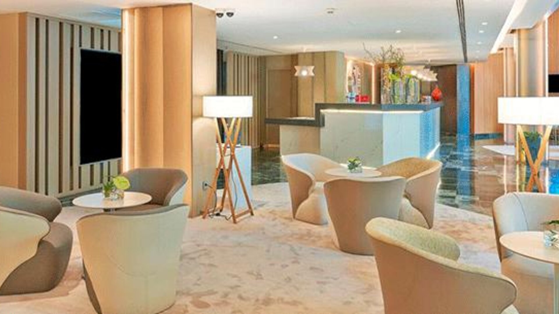 Elegant lobby seating area featuring modern armchairs, small tables and floor lamps at NH Collection Barcelona Pódium.