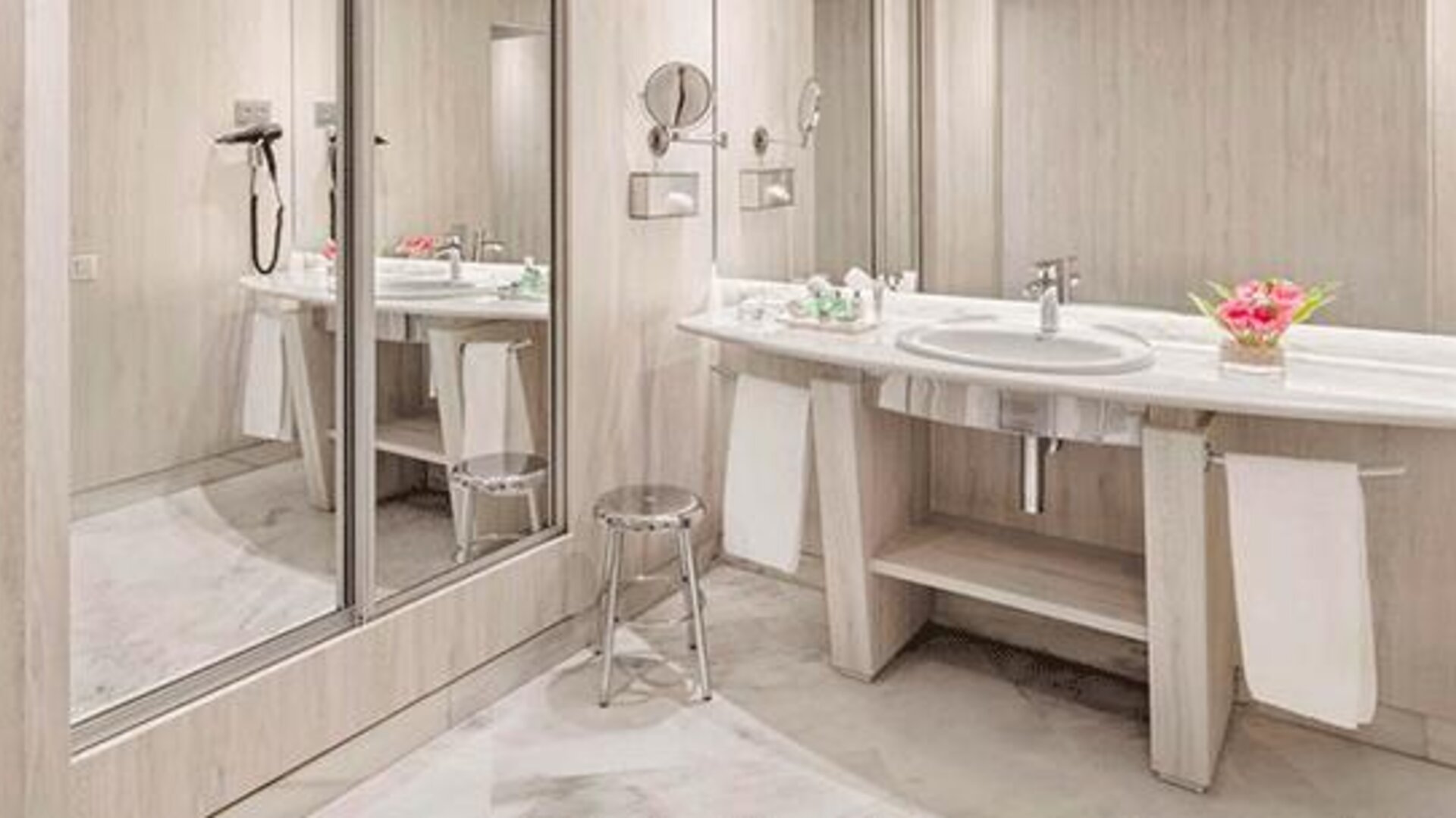 Spacious bathroom featuring a vanity, large mirrors, wall-mounted hairdryer and contemporary finishes at NH Collection Barcelona Pódium.