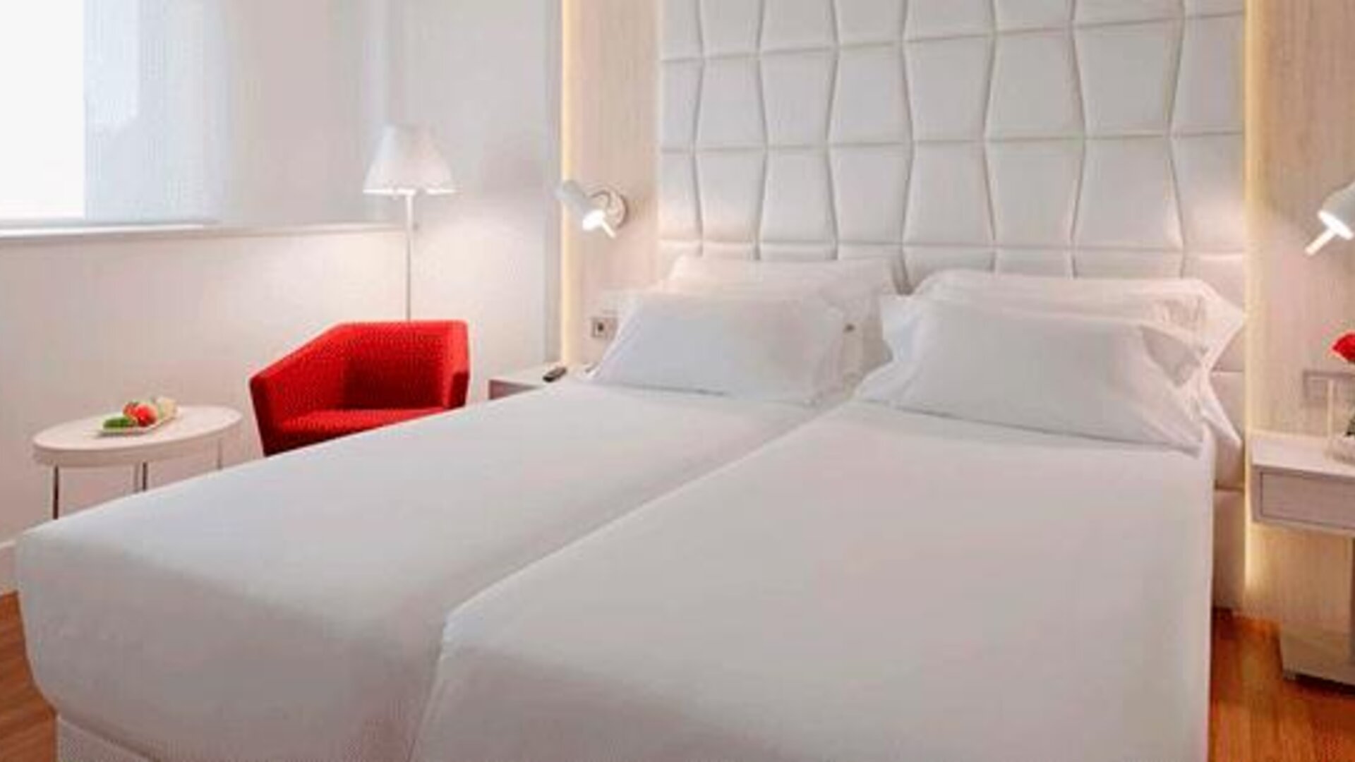 Modern guest room featuring two single beds, a red accent chair and bedside lighting at NH Collection Barcelona Pódium.