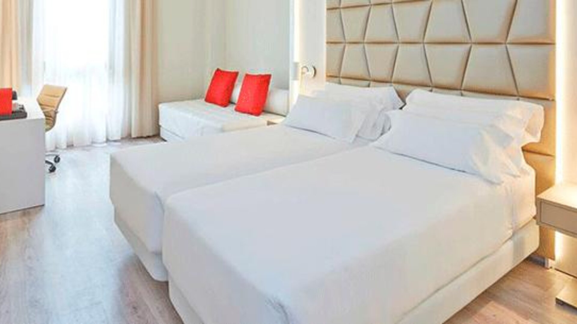 Bright guest room featuring two beds, a sofa, work desk and contemporary neutral décor at NH Collection Barcelona Pódium.