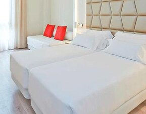 Bright guest room featuring two beds, a sofa, work desk and contemporary neutral décor at NH Collection Barcelona Pódium.
