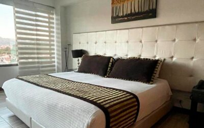 Spacious guest room featuring a king bed, seating area, polished wood flooring and large windows at Hotel Airport Travel.