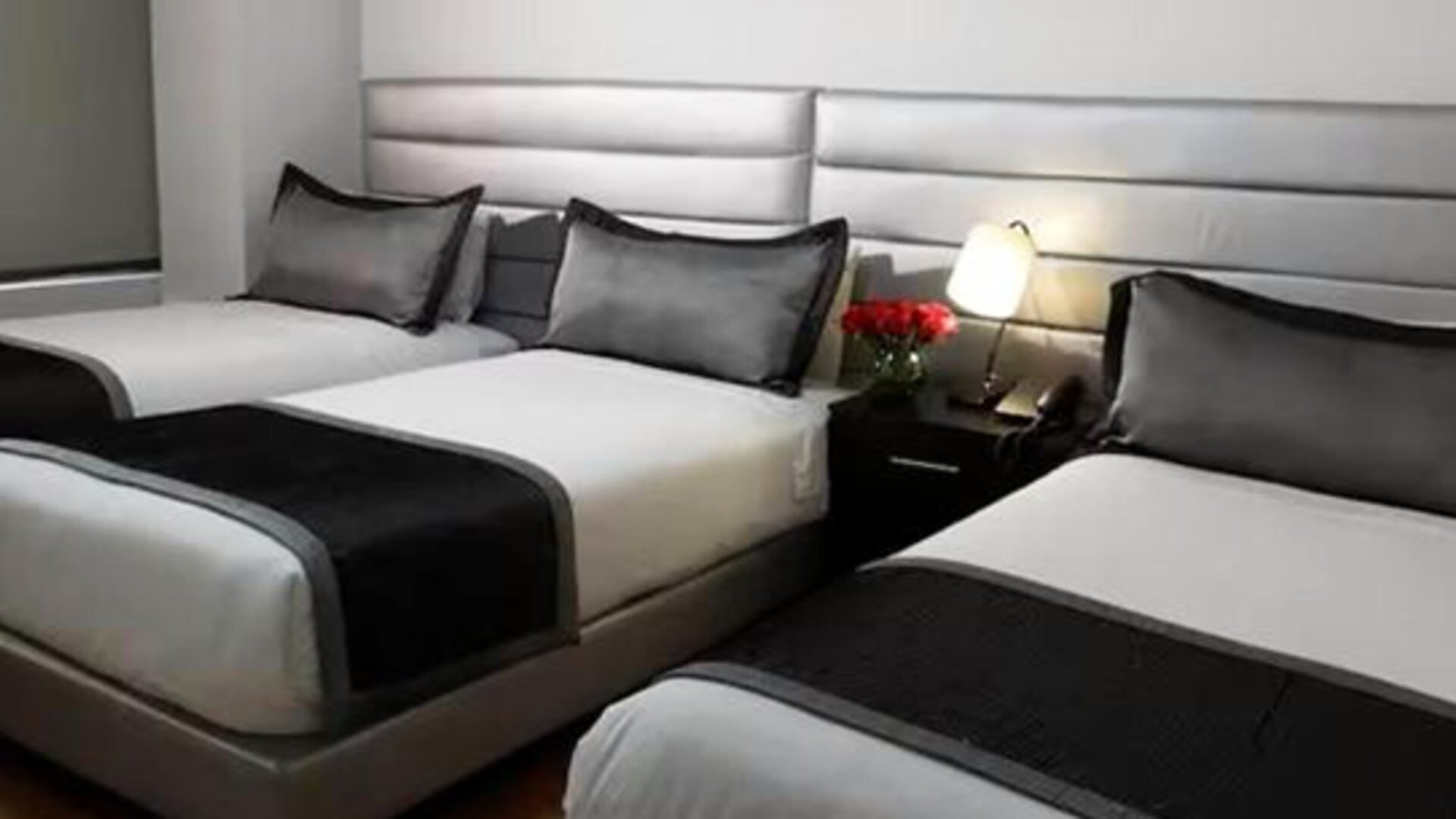 Guest room featuring three beds, coordinated black-and-white bedding and bedside lighting at Hotel Airport Travel.
