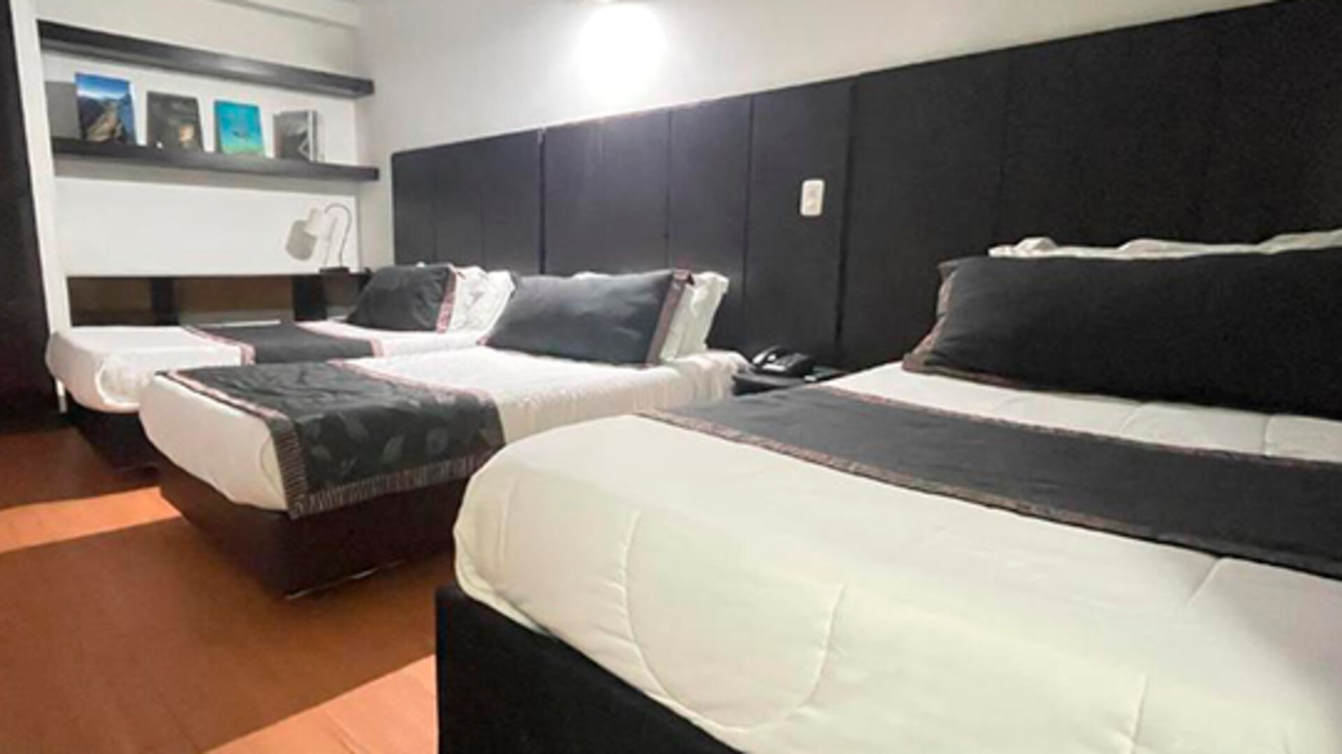 Spacious guest room featuring three beds, wood flooring and dark upholstered headboards at Hotel Airport Travel.