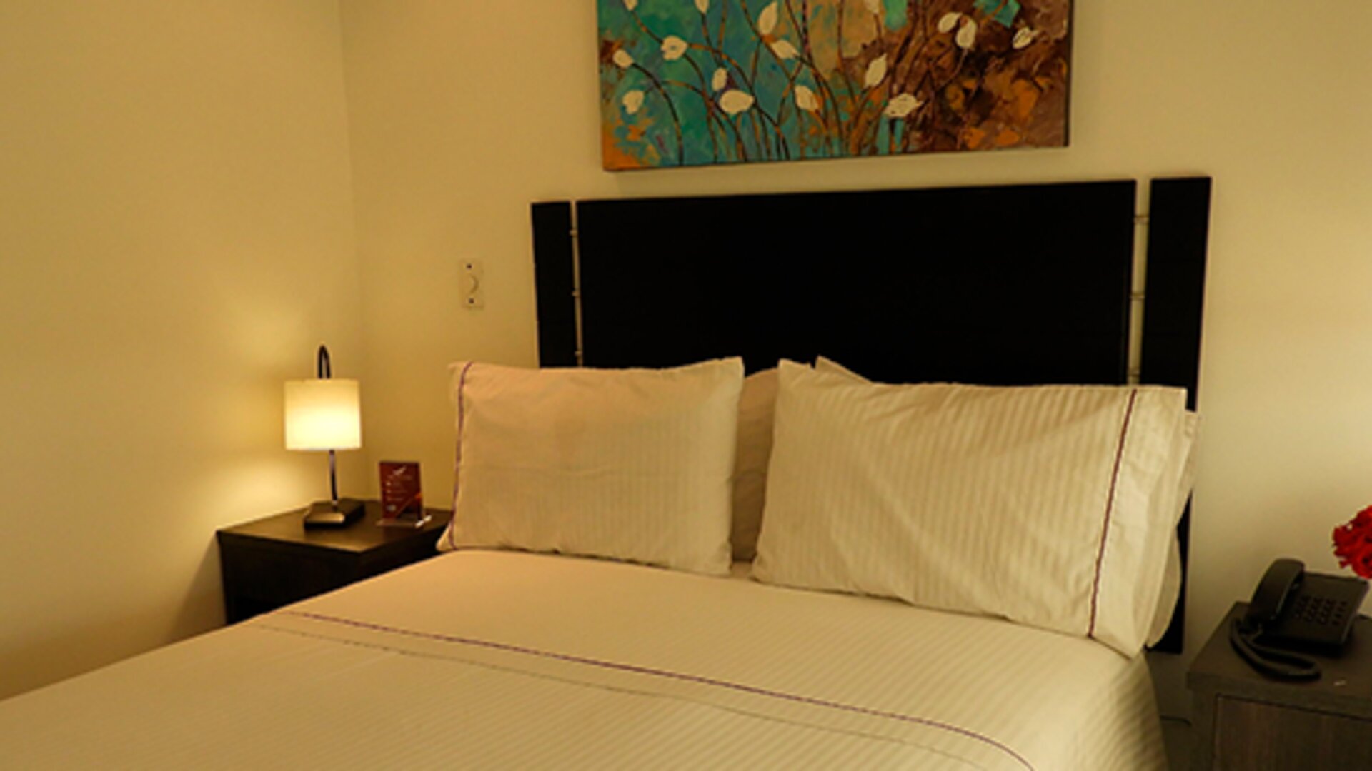 Cozy guest room featuring a double bed, bedside tables, floral arrangement and decorative wall art at Hotel Airport Travel.