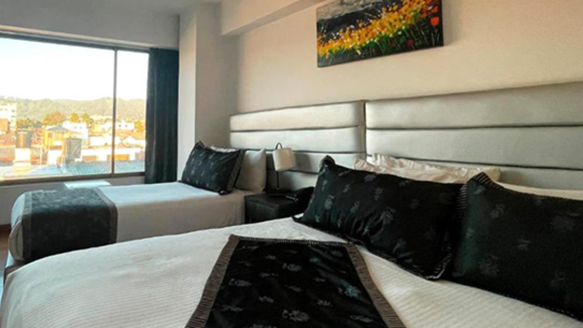 Bright guest room featuring two beds, large windows and city views at Hotel Airport Travel.