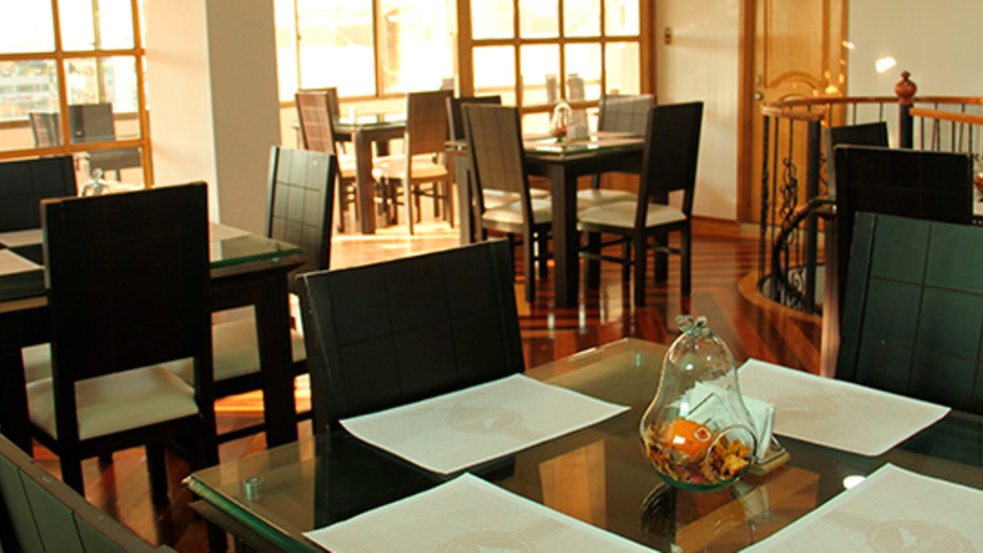 Bright dining area featuring glass-top tables, black chairs and large windows at Hotel Airport Travel.