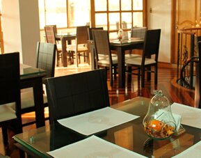 Bright dining area featuring glass-top tables, black chairs and large windows at Hotel Airport Travel.