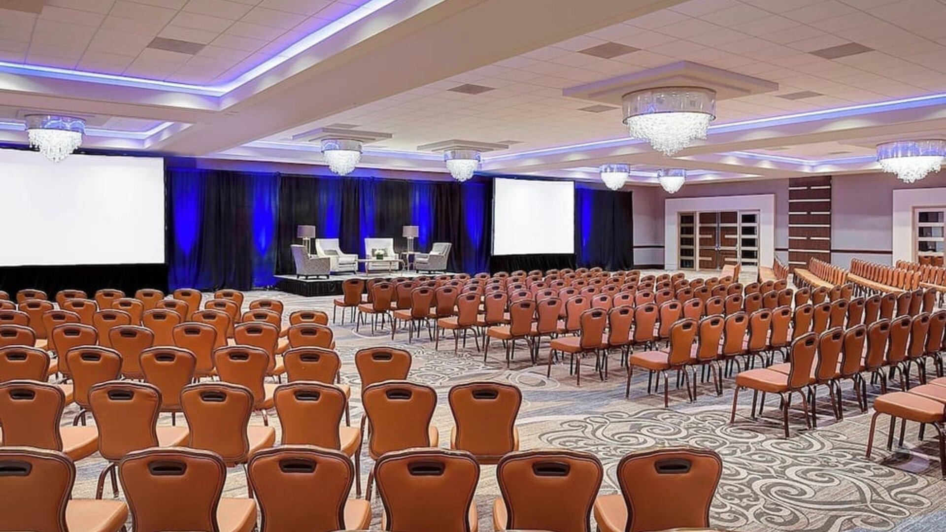 Spacious conference hall featuring theater-style seating, elegant chandeliers and a presentation stage at Sheraton Houston Brookhollow Hotel.