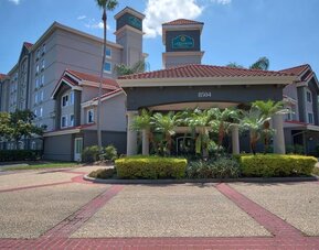 Modern hotel exterior featuring Mediterranean-inspired architecture, palm trees and a covered entrance at La Quinta Inn & Suites By Wyndham Orlando I Drive/Conv Ctr.