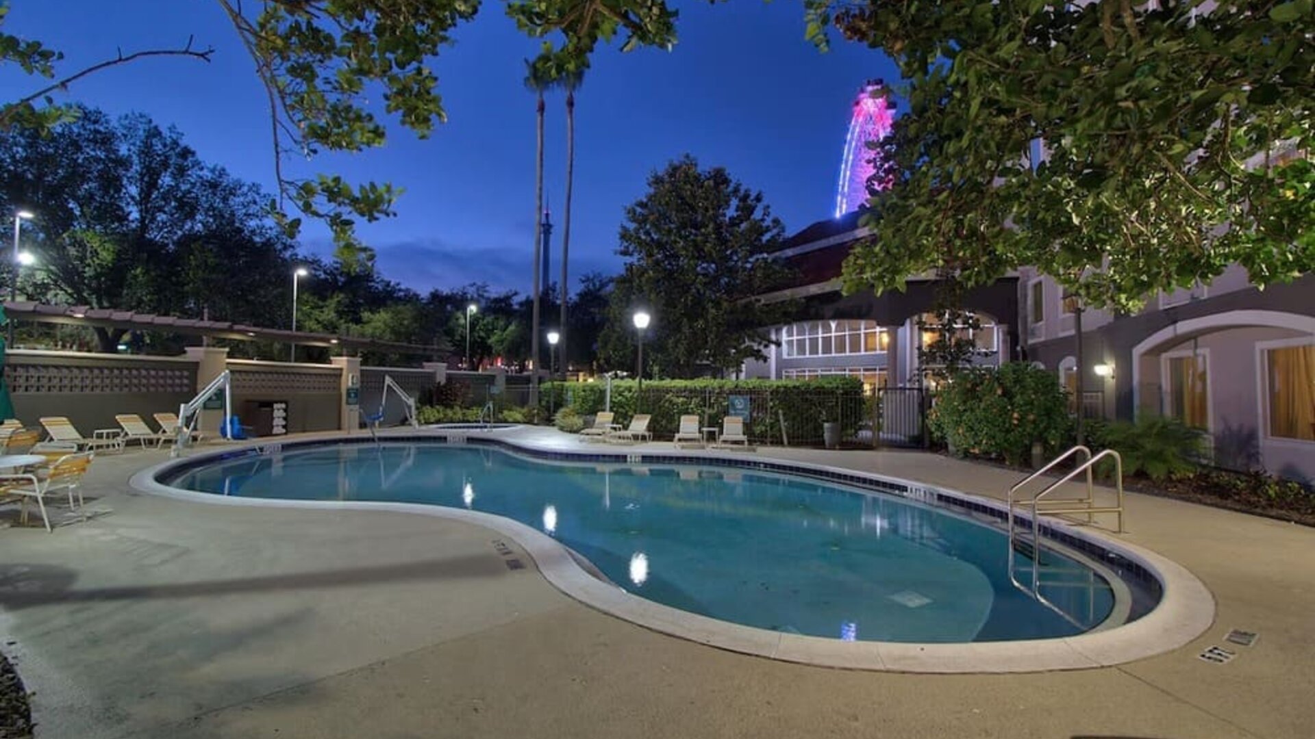 Resort-style outdoor pool featuring curved design, surrounding lounge chairs and evening views at La Quinta Inn & Suites By Wyndham Orlando I Drive/Conv Ctr.