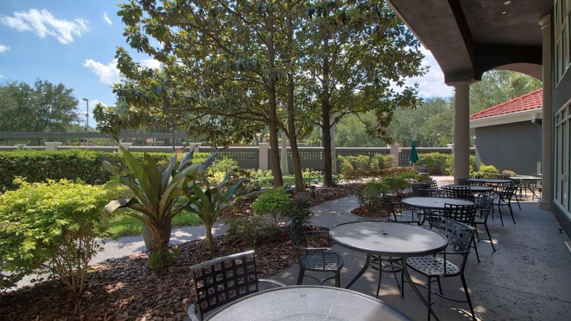 Landscaped outdoor terrace featuring shaded seating, garden views and casual dining tables at La Quinta Inn & Suites By Wyndham Orlando I Drive/Conv Ctr.