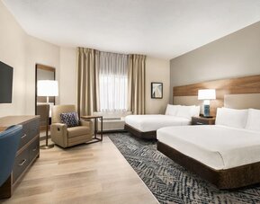 Spacious guest room featuring two beds, an upholstered armchair and a modern design at Candlewood Suites Meridian.