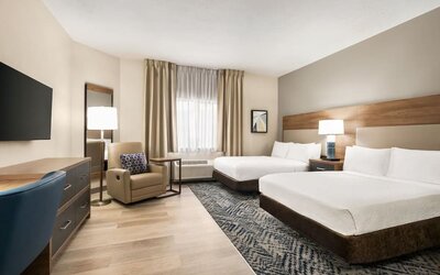 Spacious guest room featuring two beds, an upholstered armchair and a modern design at Candlewood Suites Meridian.