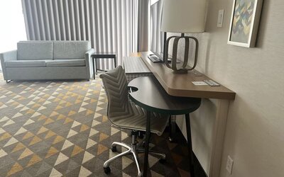 In-room workspace featuring a large desk, ergonomic seating and a comfortable lounge area with floor-to-ceiling window coverings at Holiday Inn Toronto Airport East.